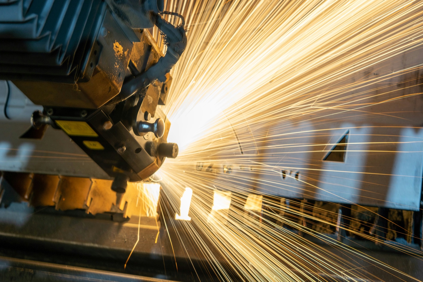 Laser cutting head throwing sparks across sheet steel